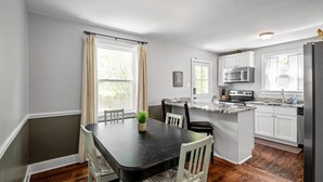 Een moderne keuken met witte kastjes, een zwart aanrecht en een eethoek met een donkere tafel en witte stoelen.
