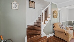 Een trap met houten treden en witte leuningen, een beige fauteuil met een kussen, en een decoratief wandobject.