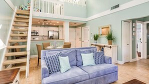 A spacious living area with a blue sofa, a wooden staircase, a kitchen, and a dining area. - Headline (Sanibel)