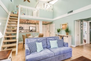 A spacious living area with a blue sofa, a wooden staircase, a kitchen, and a dining area.