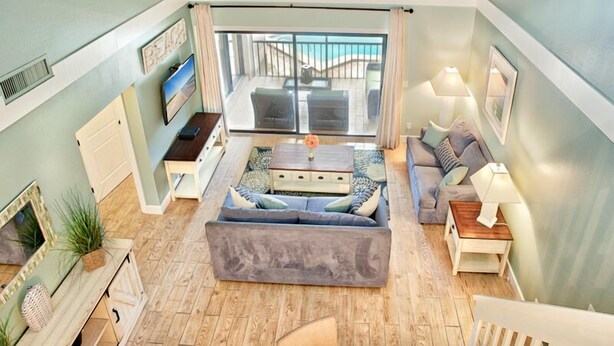 A spacious living room with a large sofa, a coffee table, and a TV. There is a balcony with a view of the city. - Headline (Sanibel)