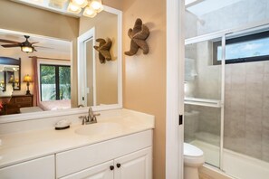 A bathroom with a white vanity, a large mirror, a ceiling fan, and a glass-enclosed shower.