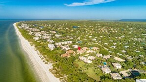 An aerial view of a coastal residential area with houses, a beach, and a clear sky. - Headline (Sanibel)