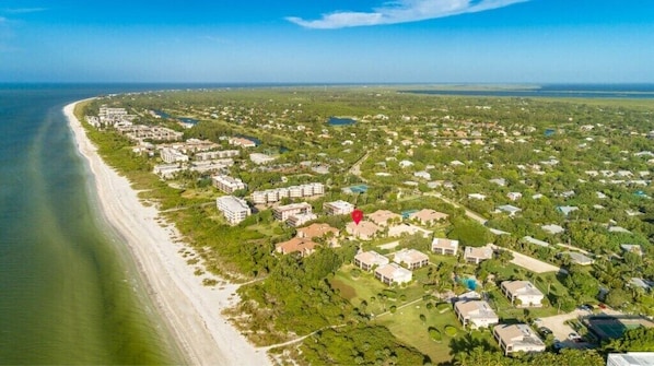 Vue aérienne d’une zone résidentielle côtière, avec des maisons, une plage et un ciel dégagé.