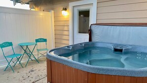 A hot tub in front of a house with a wooden deck, a door, and a window.