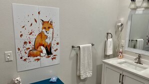 A bathroom with a white sink, a mirror, a towel rack, and a painting of a fox.