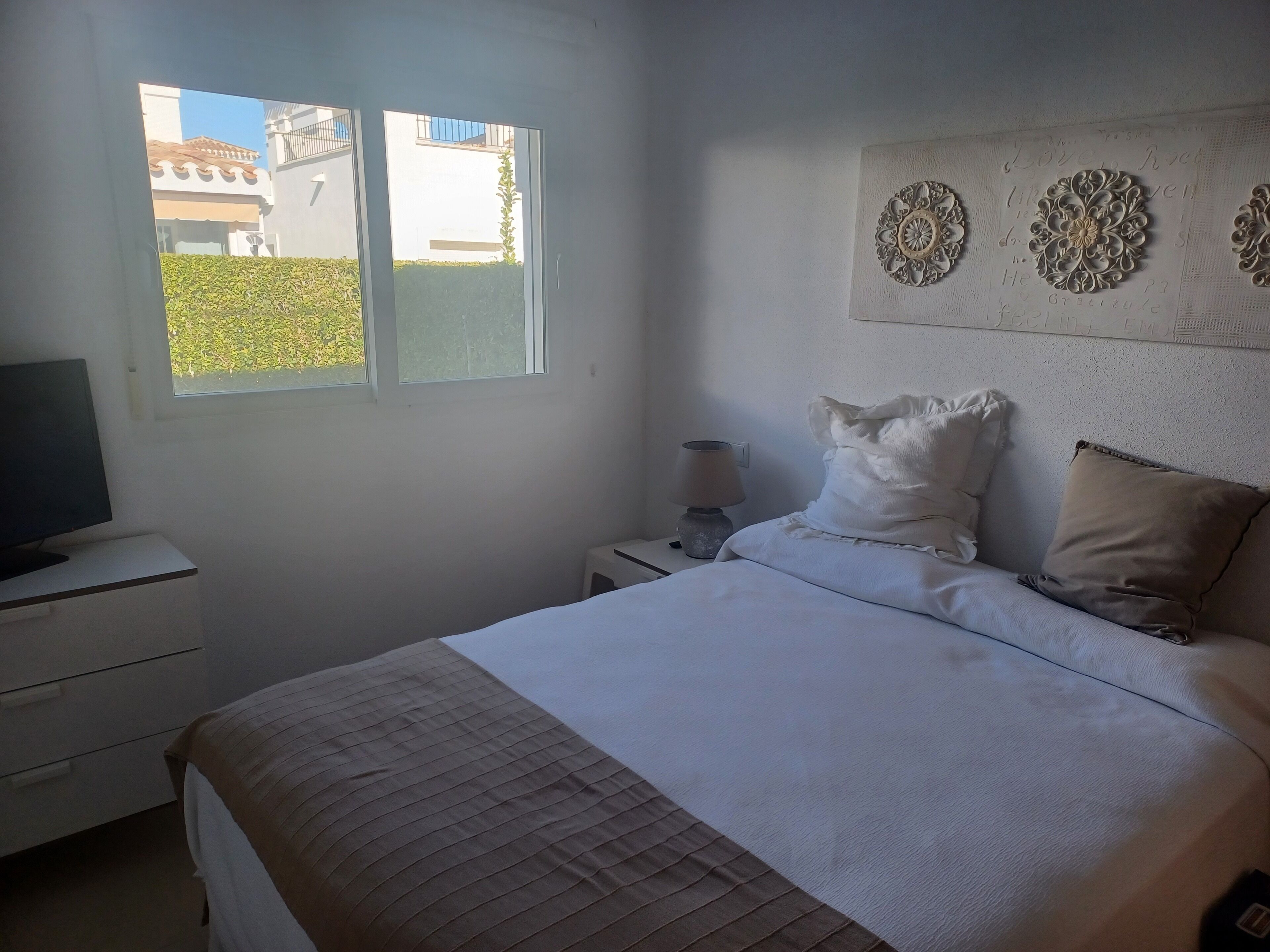Quarto com uma cama, mesa de cabeceira com abajur, televisão e decoração na parede.