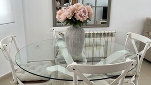 Une table ronde en verre, des chaises blanches, un vase avec des fleurs et un miroir au mur.
