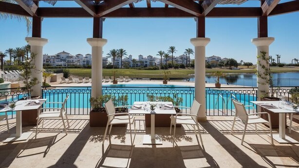Un espace extérieur aménagé, abrité et doté de sièges, avec vue sur la piscine, comprenant des chaises et des tables blanches.