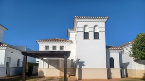 Un bâtiment blanc avec un toit en tuiles, une petite tour dotée de fenêtres en arc de cercle et un patio couvert.