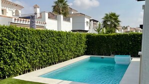 Une piscine entourée d’une pelouse bien entretenue et d’une haie imposante.