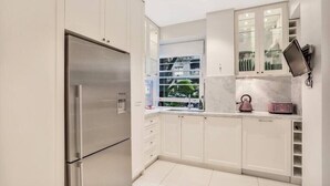 A modern kitchen with white cabinetry, a stainless steel refrigerator, and a window with a view of greenery.