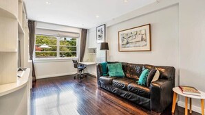 A modern living room with a leather sofa, a desk, and a large window with curtains.