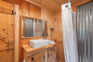 Ein Badezimmer aus Holz mit einem weißen Waschbecken, einem Spiegel und einer Duschvorhang.