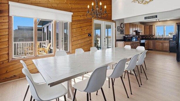 A dining area with a large table and chairs, wooden walls, and a view of the outside. - Cair Paravel | 680 ft to the beach | (Virginia Beach)