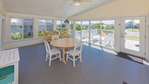 A covered outdoor dining area with a round table and chairs, large windows, and a view of the surrounding landscape. - Cair Paravel | 680 ft to the beach | (Virginia Beach)