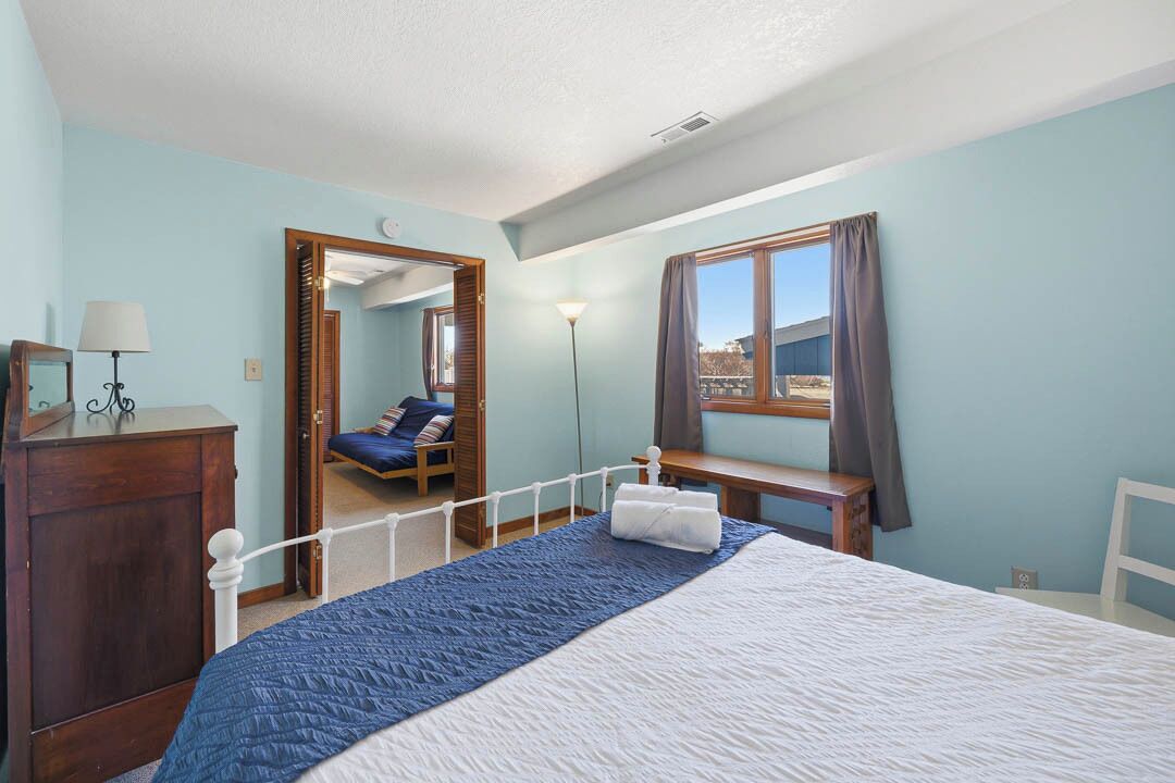 A bedroom with a bed, a desk, a chair, a mirror, a lamp, and a window.