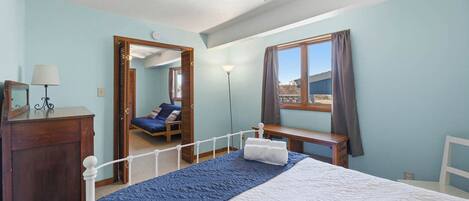 A bedroom with a bed, a desk, a chair, a mirror, a lamp, and a window.