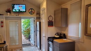 A compact kitchen with a refrigerator, stove, and oven. A television displaying a pollen forecast is mounted on the wall.