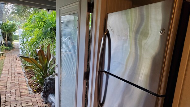 A stainless steel refrigerator with a handle, a sliding glass door, and a metal kick plate.