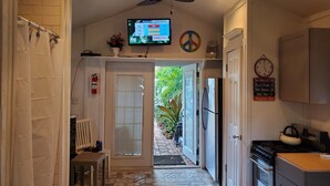 A kitchen with a TV displaying pollen forecast, a clock, and a door leading to a patio.