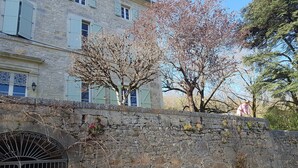 A stone wall with a metal gate, a tree with bare branches, and a building with light-colored stone walls and shutters. - Large vacation home in the Lot in the heart of the Quercy regional park (Saint-Sulpice)
