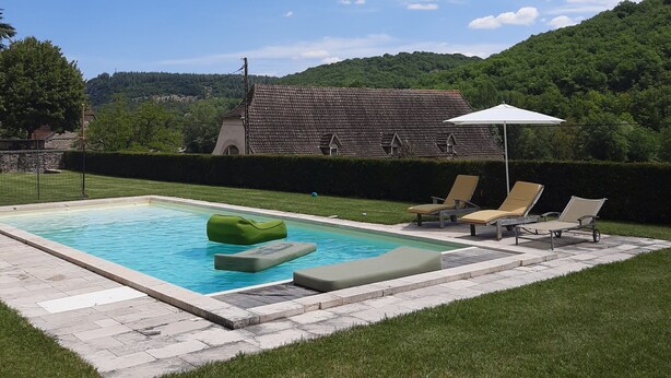 A swimming pool with lounge chairs and a sun umbrella, surrounded by a well-maintained lawn and a building with a tiled roof. - Large vacation home in the Lot in the heart of the Quercy regional park (Saint-Sulpice)