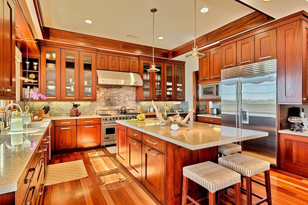 A spacious kitchen with wooden cabinets, a large island, stainless steel appliances, and a hanging light fixture.