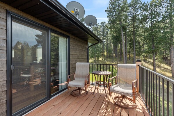 Relax on the deck with a view of the forest, surrounded by a wooden railing and comfortable seating for two.