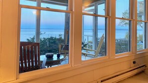 A room with large windows overlooking a body of water, a wooden deck with outdoor furniture, and a ceiling fan. - WATERFRONT Maine Historical Cottage with Separate Guest Cottage (Northport)