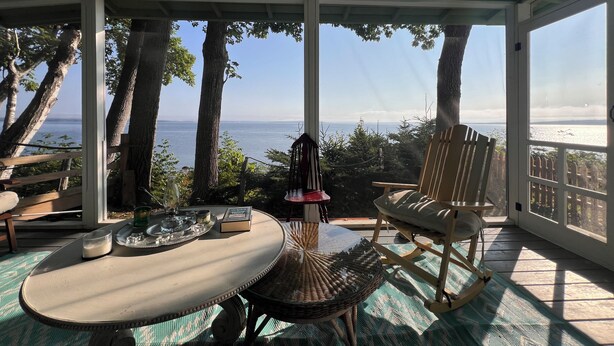 A covered outdoor seating area with a table, chairs, and a view of the sea. - WATERFRONT Maine Historical Cottage with Separate Guest Cottage (Northport)
