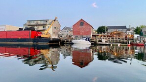 A waterfront scene with a docked boat, a red barn, and industrial buildings. - WATERFRONT Maine Historical Cottage with Separate Guest Cottage (Northport)