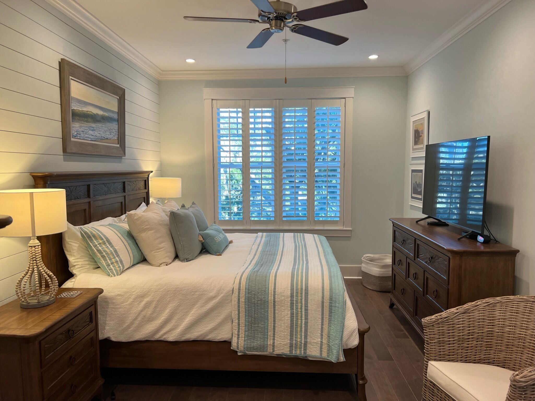 A bedroom with a bed, nightstands, a dresser, a television, a ceiling fan, and a window with blinds.