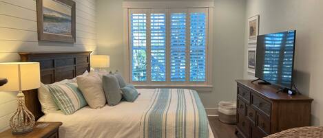 A bedroom with a bed, nightstands, a dresser, a television, a ceiling fan, and a window with blinds.