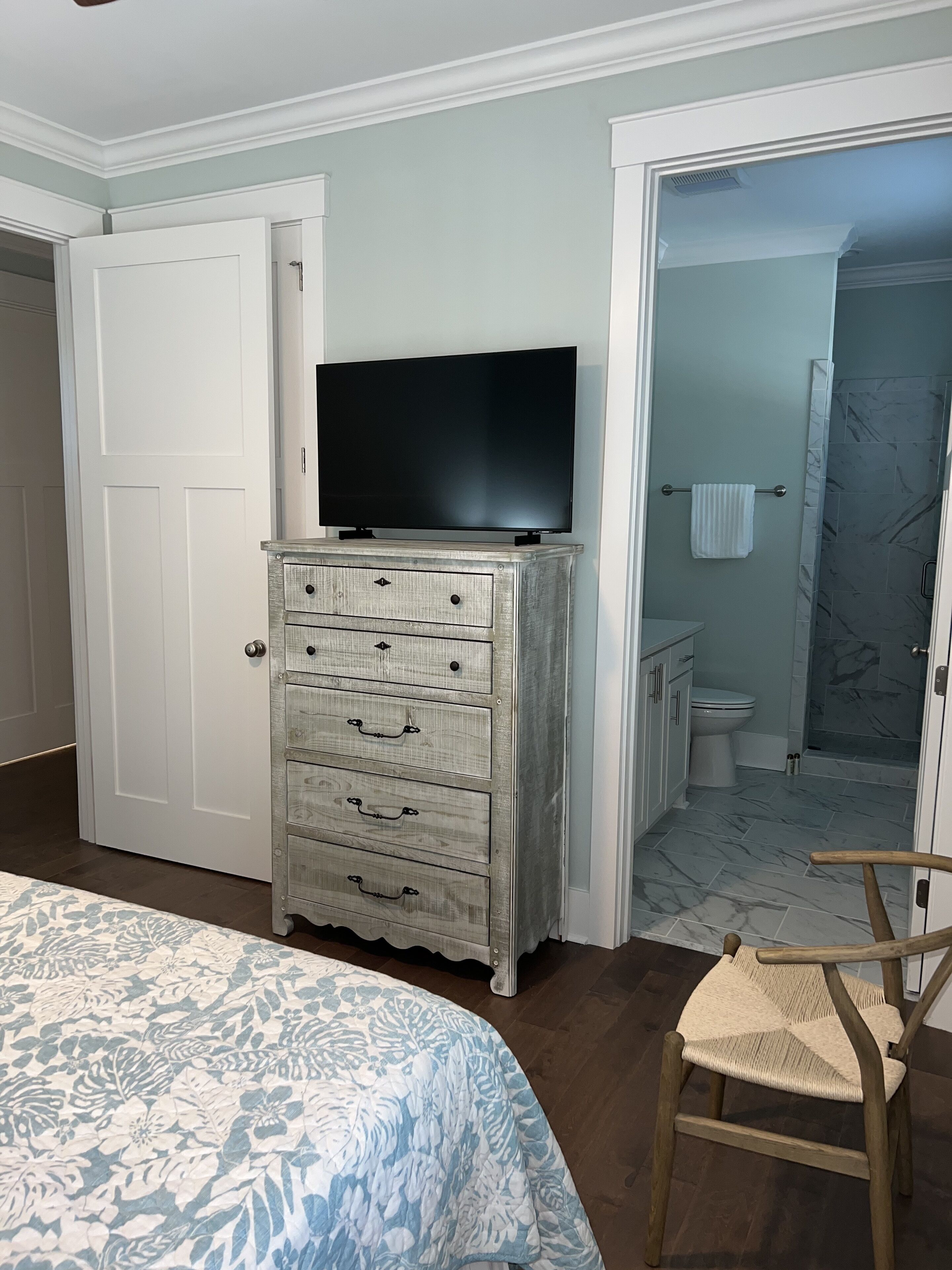 A bedroom with a bed, a dresser, a television, and a bathroom visible through an open door.