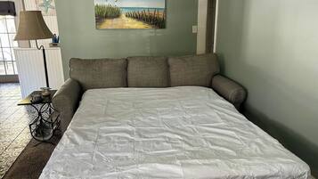 A bedroom with a large bed, a painting of a beach scene, and a lamp on a side table.