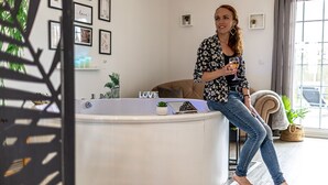 A woman sitting by a bathtub in a well-lit room with framed pictures on the wall and a window with curtains. - Suite L'échappée - Romantic home - Private SPA (PEZARCHES)