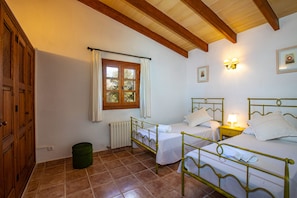 A room with two single beds, a wooden door, a window with curtains, a radiator, and a wall-mounted light fixture.