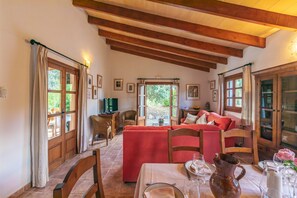A cozy room with a dining table set for two, wooden beams on the ceiling, and a red sofa.