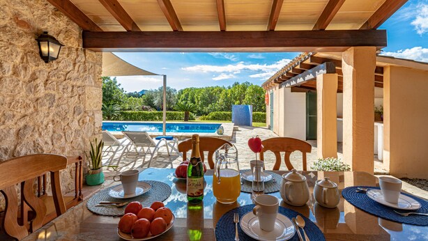 A dining table set with plates, cups, and a bottle of wine, overlooking a pool and lush greenery. - Lovely villa in Pollensa countryside (Pollensa / Pollença)