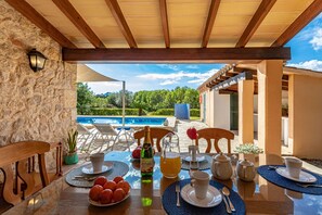 A dining table set with plates, cups, and a bottle of wine, overlooking a pool and lush greenery.