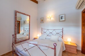A bedroom with a metal-framed bed, bedside tables with lamps, a large mirror, and a wall-mounted light fixture.