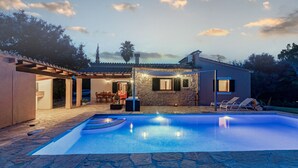 A swimming pool with stone tiles, a covered patio with outdoor furniture, and a stone building with a stone facade.