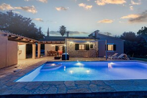 A swimming pool with stone tiles, a covered patio with outdoor furniture, and a stone building with a stone facade.