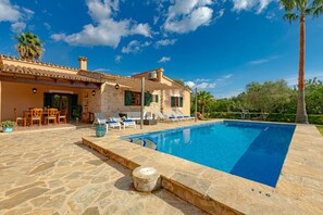 A pool area with stone flooring, lounge chairs, and a building with a tiled roof.