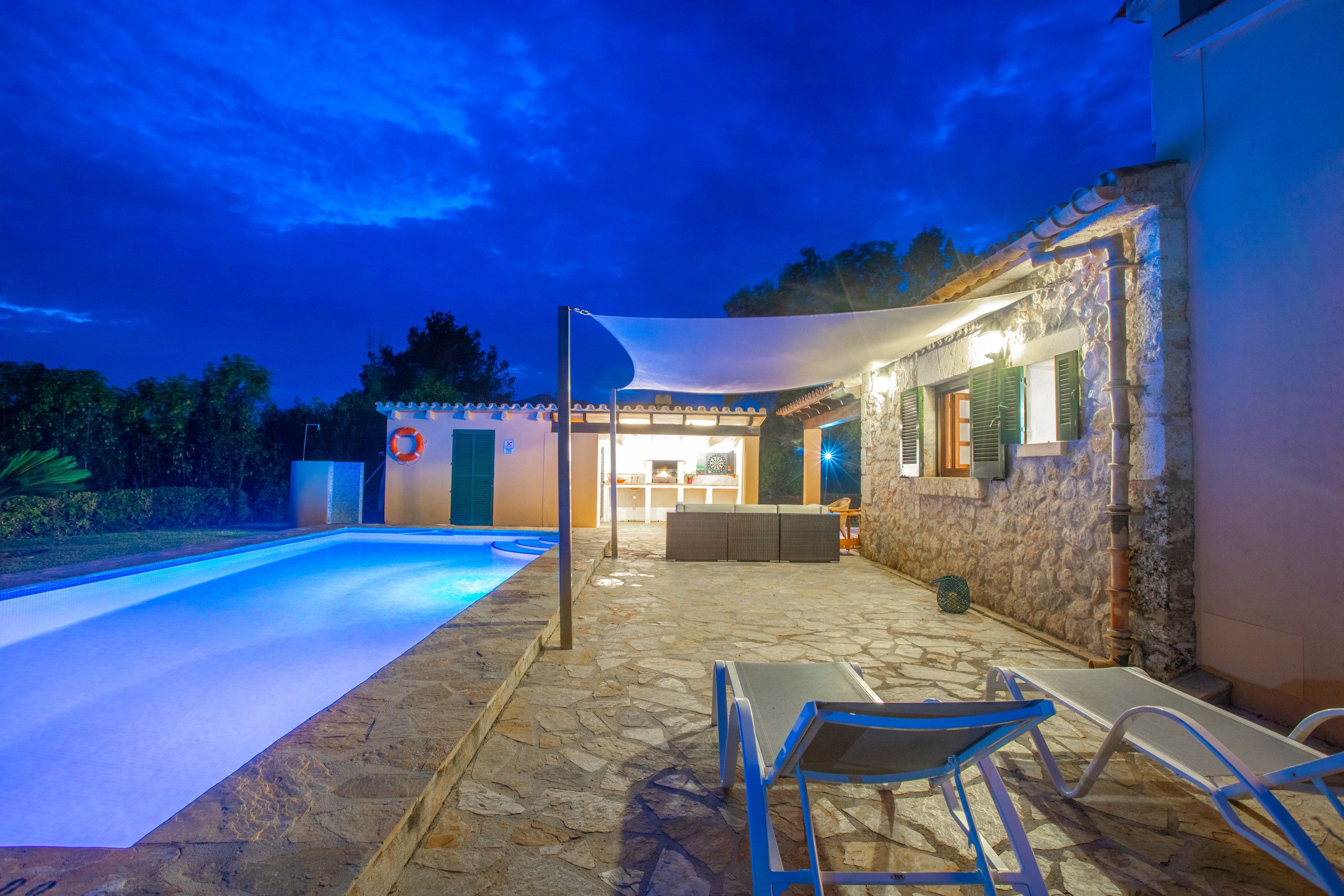 Un espace extérieur dallé de pierre, doté d’une piscine, de chaises longues et d’un coin salon abrité avec une table et des chaises.