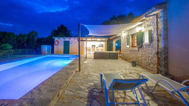 A stone-floored outdoor area with a pool, lounge chairs, and a covered seating area with a table and chairs.