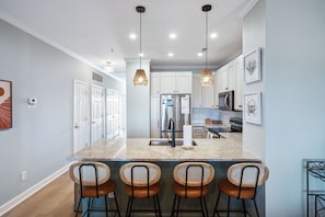A modern kitchen with a central island, bar stools, pendant lighting, and stainless steel appliances.