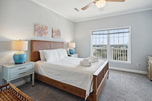 A bedroom with a large bed, two bedside tables, a ceiling fan, and a window with a view.