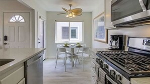 A kitchen with a stove, microwave, and ceiling fan. There is a dining table with chairs and a window with blinds.